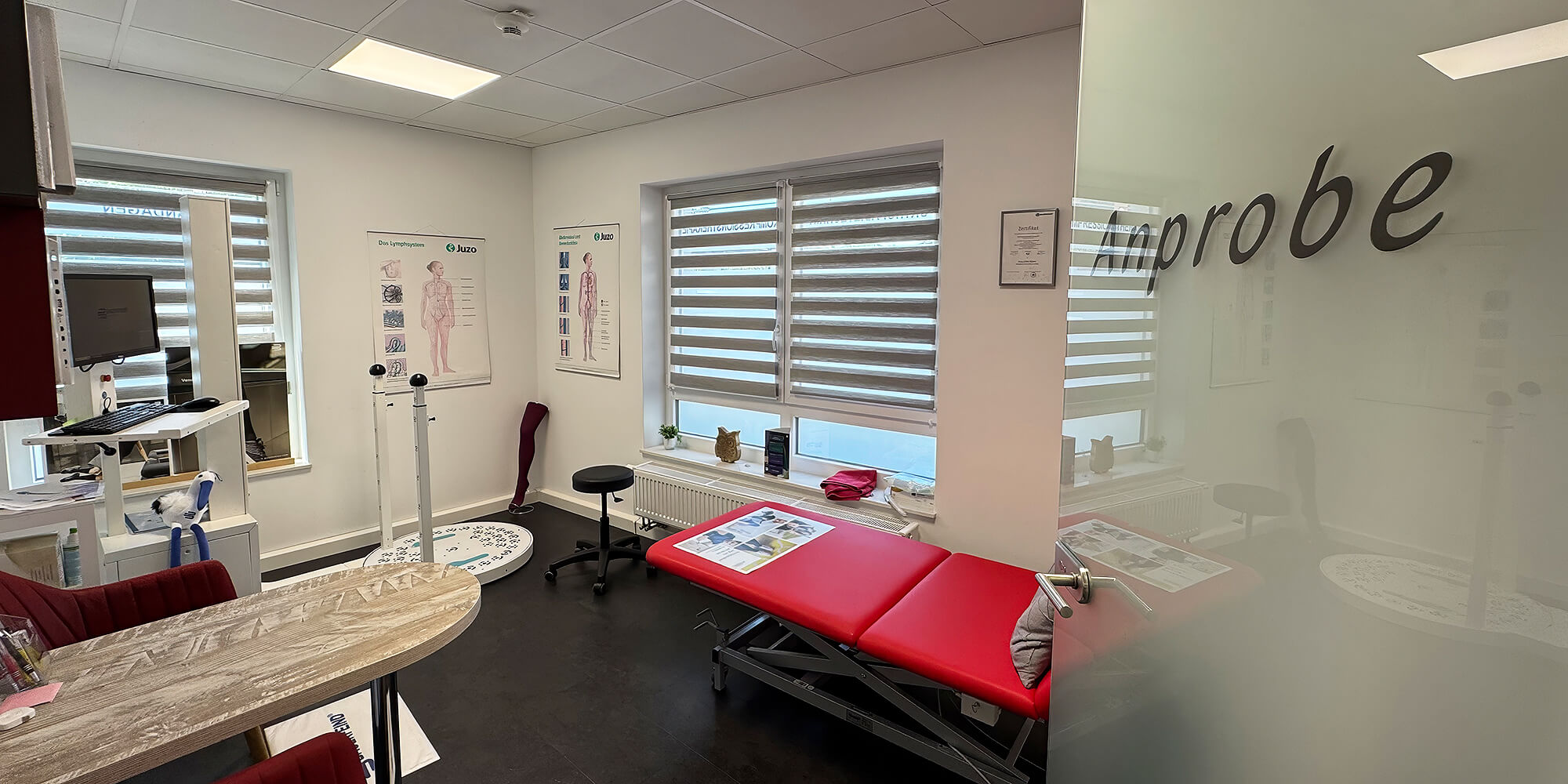 Behandlungsraum mit roter Therapieliege, Messgeräten und anatomischen Schautafeln in einer Orthopädietechnik-Praxis
